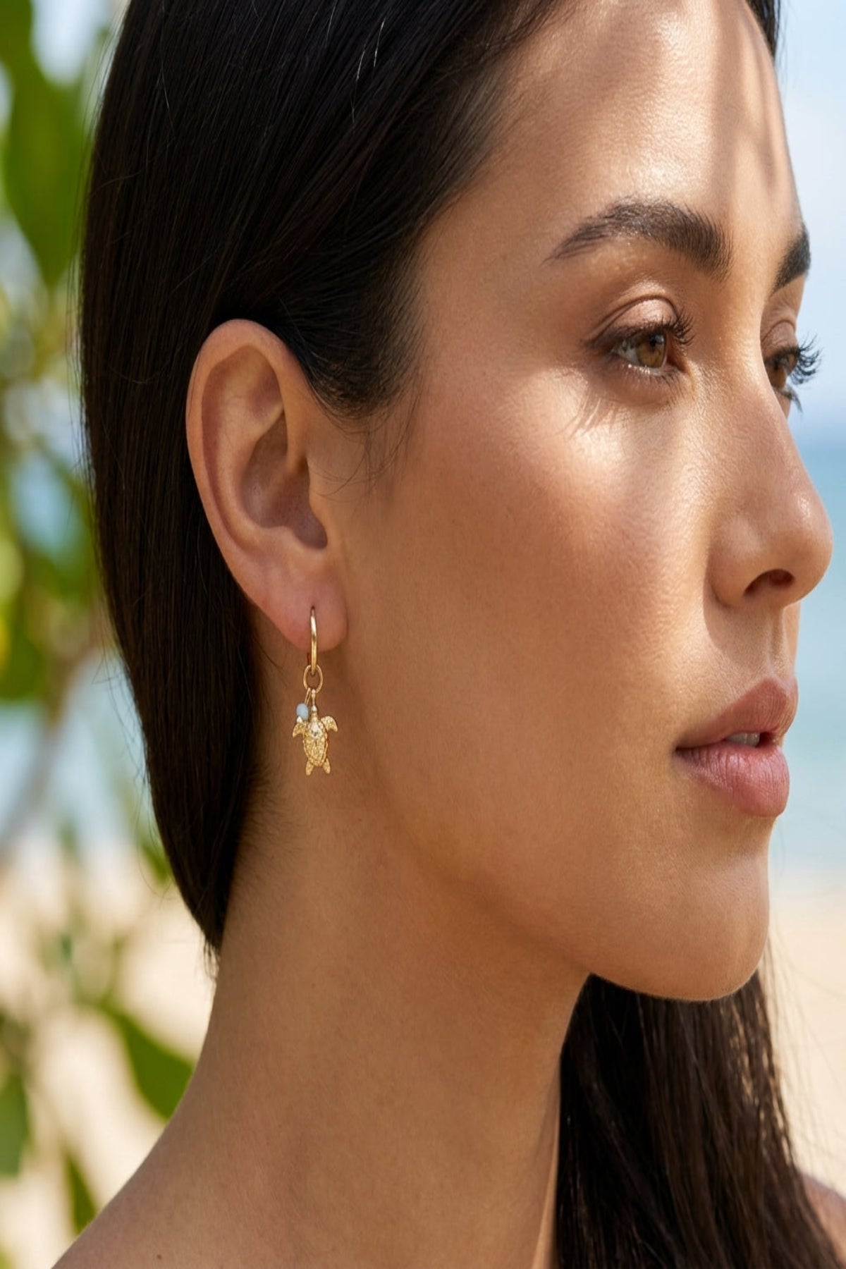 Close-up of delicate turtle-shaped stainless steel earrings with gold finish on a textured wooden surface