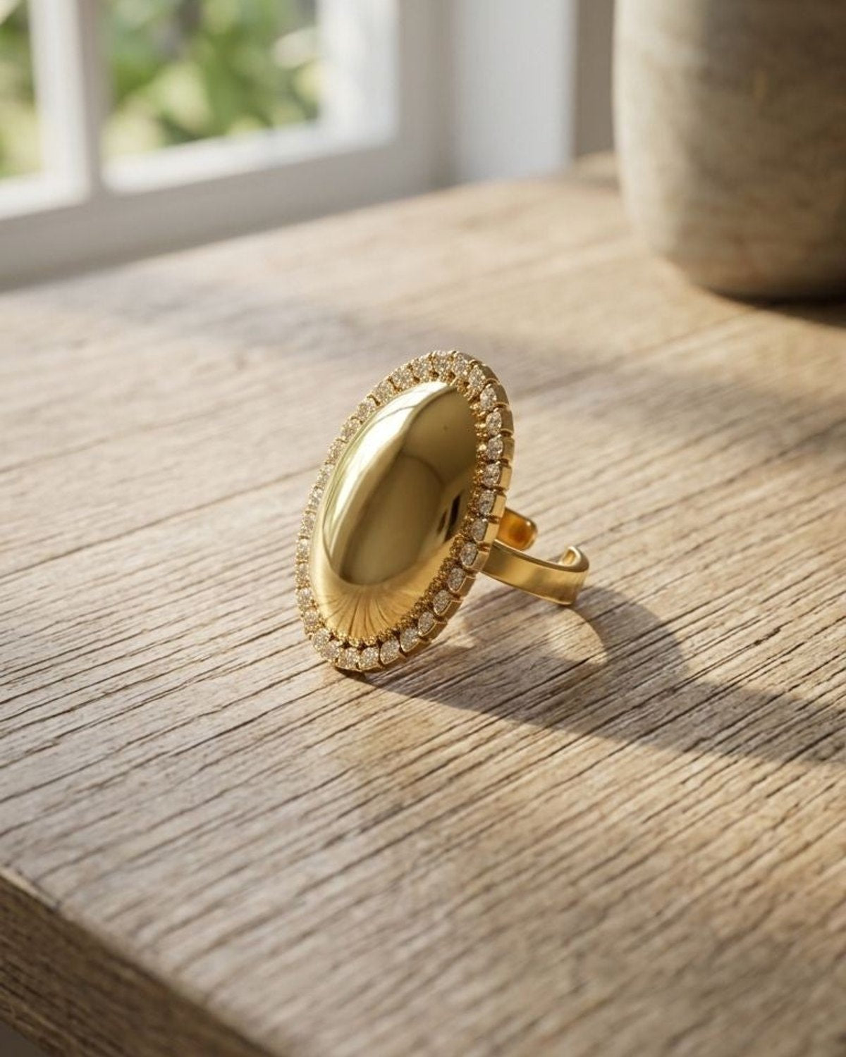 Close-up of Golden Oval Statement ring with rhinestone border on textured wood, emphasizing its high-shine finish and intricate details.