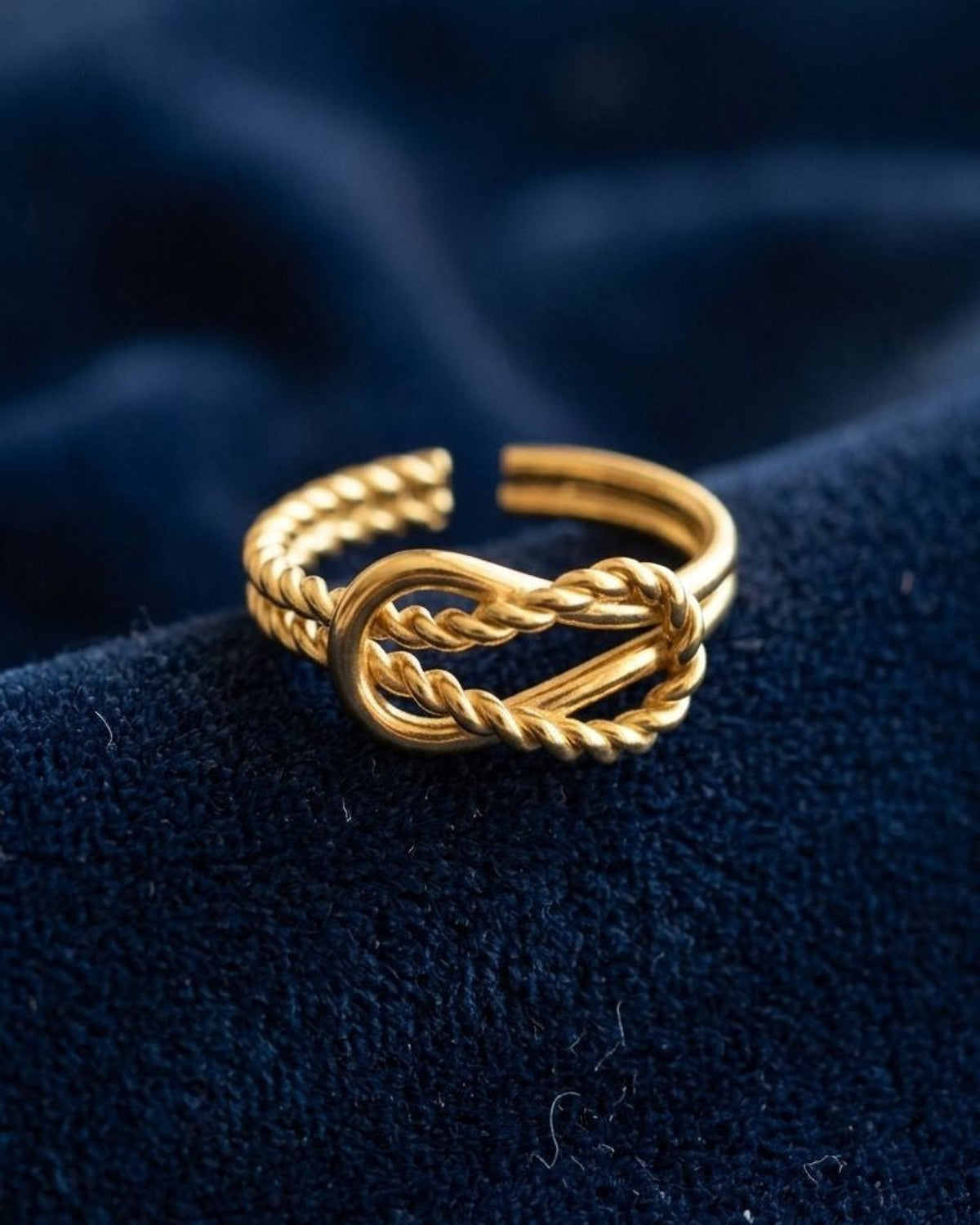 Close-up of Golden Twisted Knot stainless steel ring resting on textured velvet fabric, highlighting its polished finish and intricate twisted knot detail.