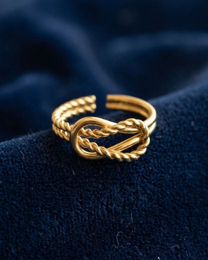 Close-up of Golden Twisted Knot stainless steel ring resting on textured velvet fabric, highlighting its polished finish and intricate twisted knot detail.