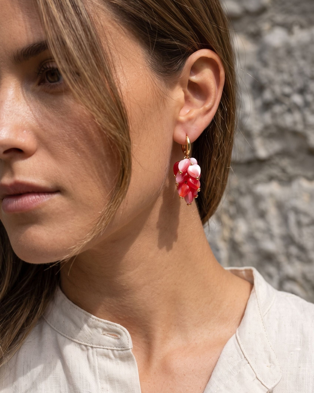Petite heart-shaped acrylic bead earrings with stainless steel hooks resting on a weathered grey limestone surface.