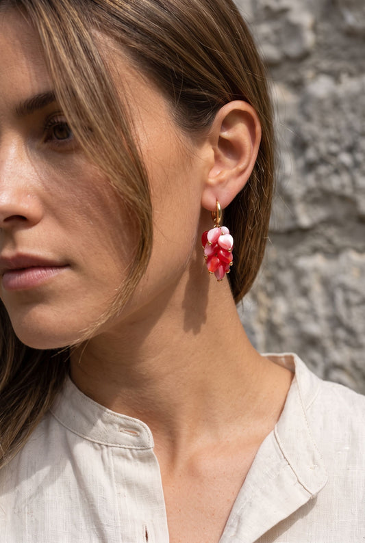 Petite heart-shaped acrylic bead earrings with stainless steel hooks resting on a weathered grey limestone surface.