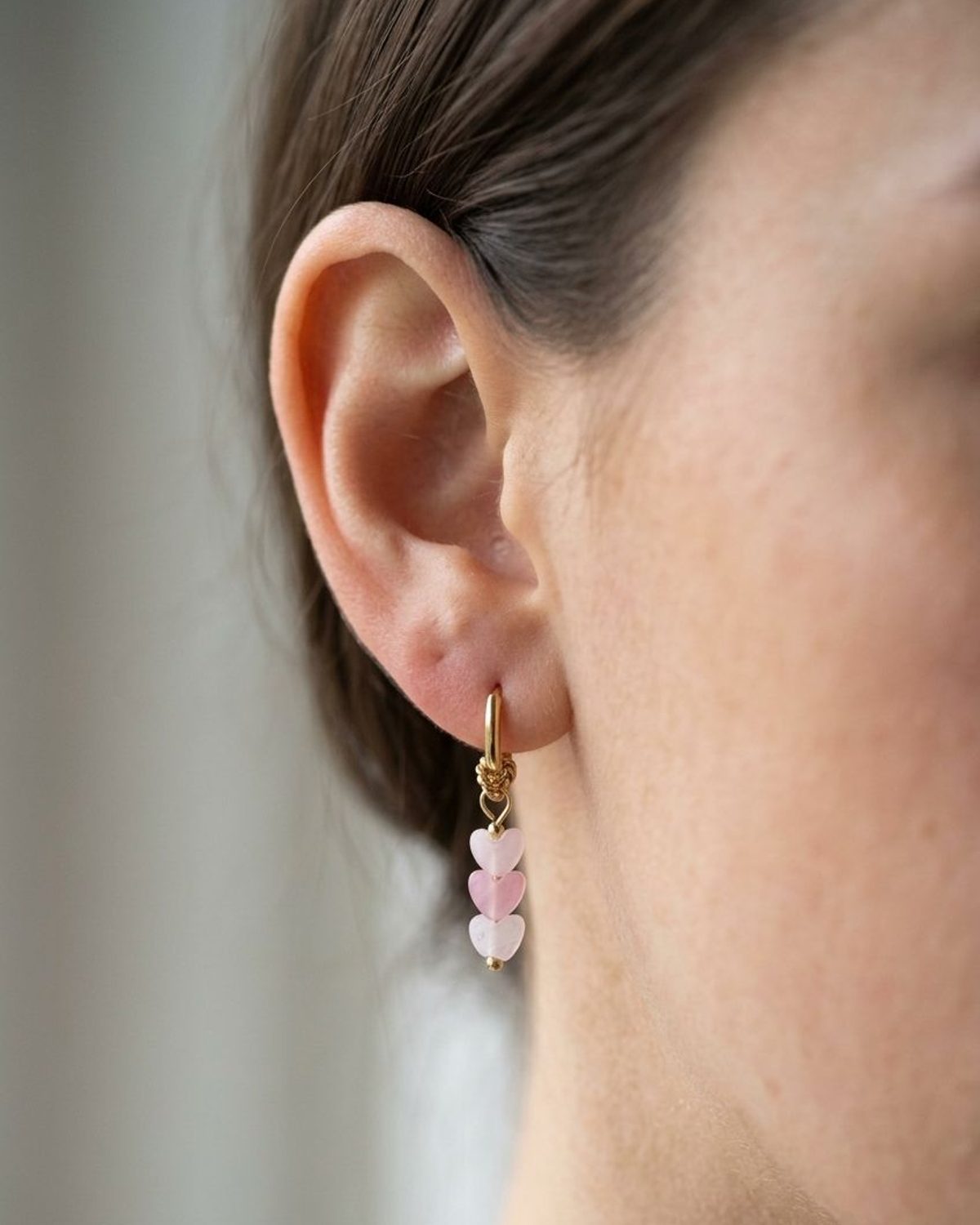 Dainty stainless steel hoop earrings featuring dangling pebbled opal heart charms worn on an earlobe.