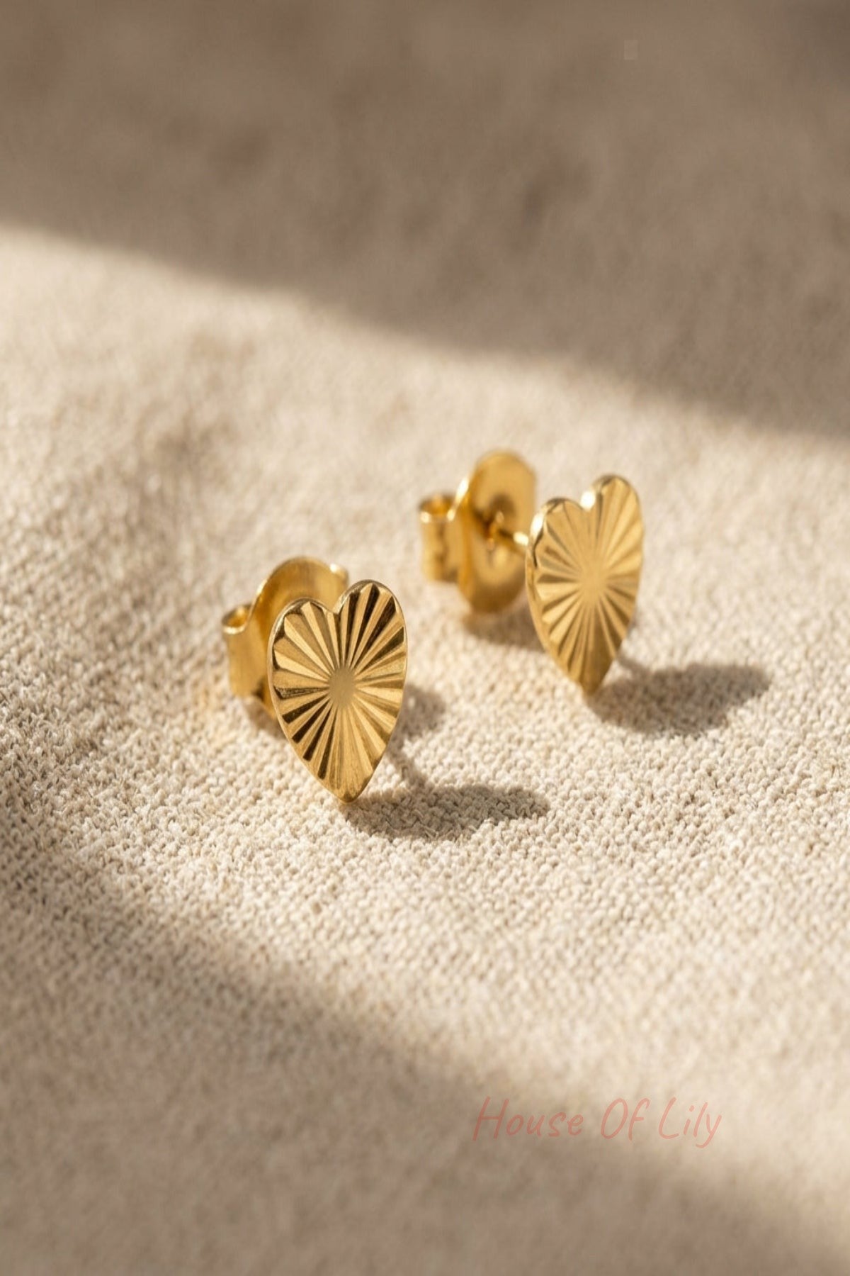 Close-up of small stainless steel heart-shaped earrings with intricate pattern, on soft fabric background, highlighting fine details and true silver hue.