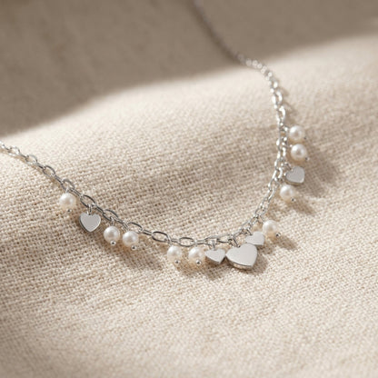 High-resolution macro image of the Hearts & Pearls Pendant Necklace, showcasing tiny heart-shaped charms and faux pearls on a soft fabric background with fine craftsmanship details.
