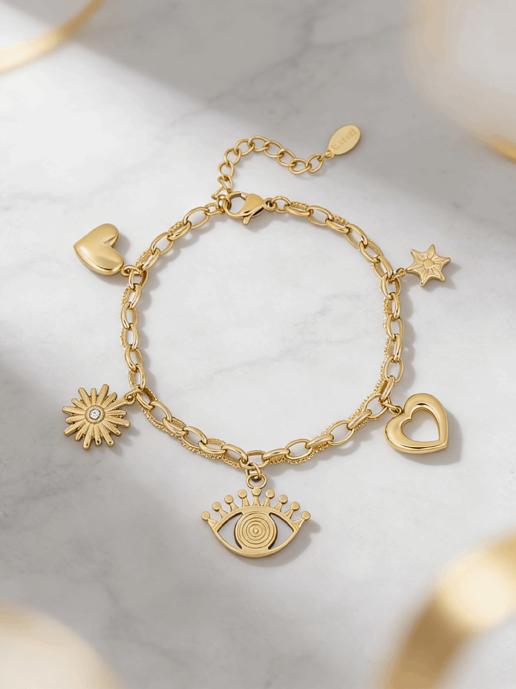 Gold charm bracelet featuring evil eye, heart, sun, and star charms on a textured link chain against marble.