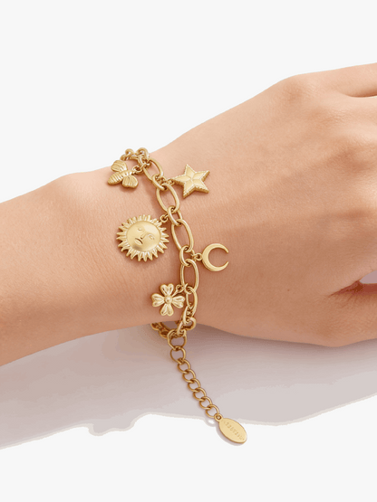 Gold-tone charm bracelet featuring sun, moon, star, butterfly, and flower charms on an oval-link chain on a wrist.