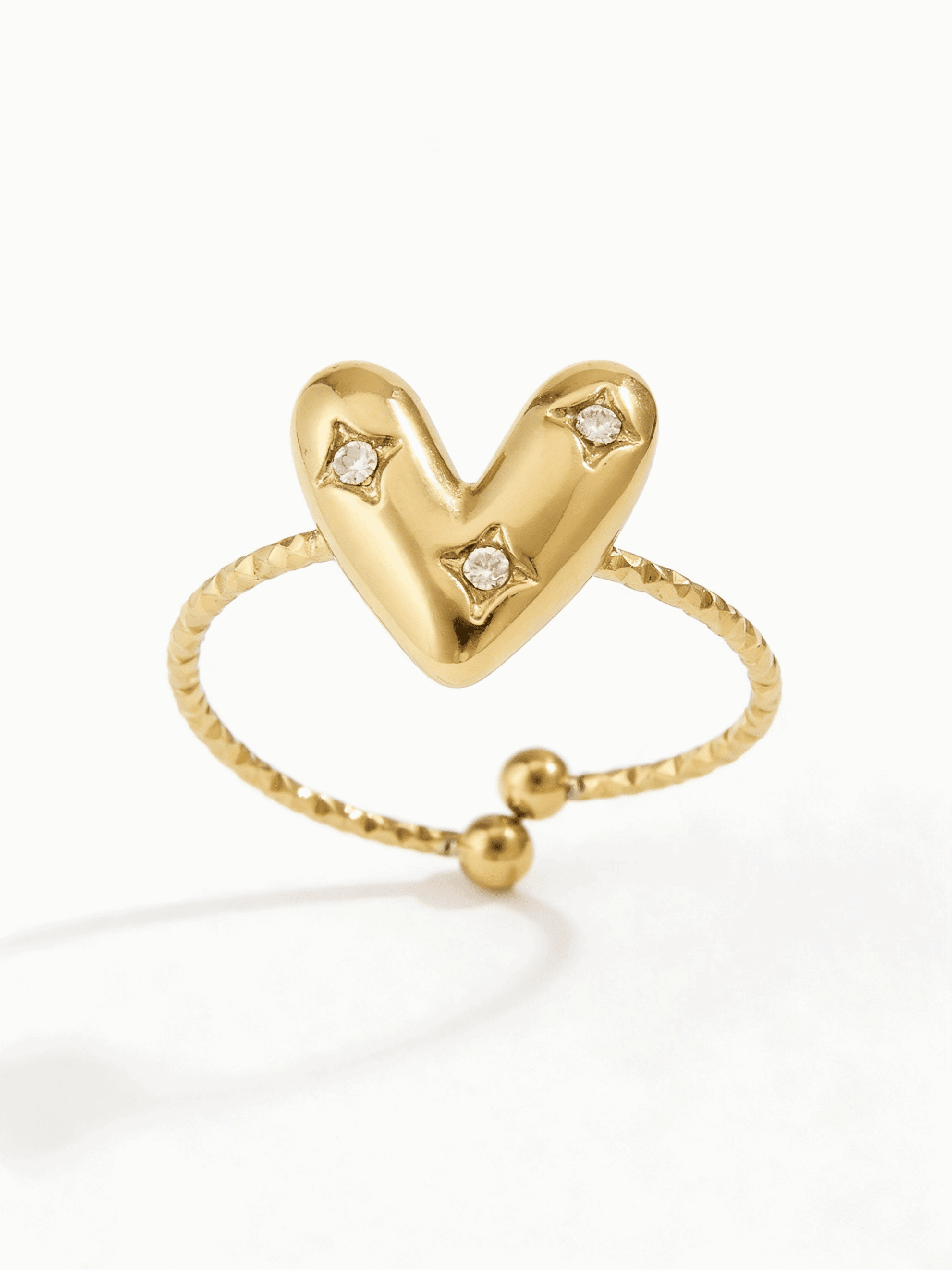 Gold-tone adjustable ring featuring a puffy heart center with three small inlaid crystals on a textured band.