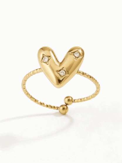 Gold-tone adjustable ring featuring a puffy heart center with three small inlaid crystals on a textured band.