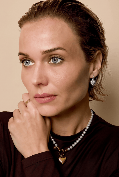 Woman wearing a pearl necklace and earrings against a beige background