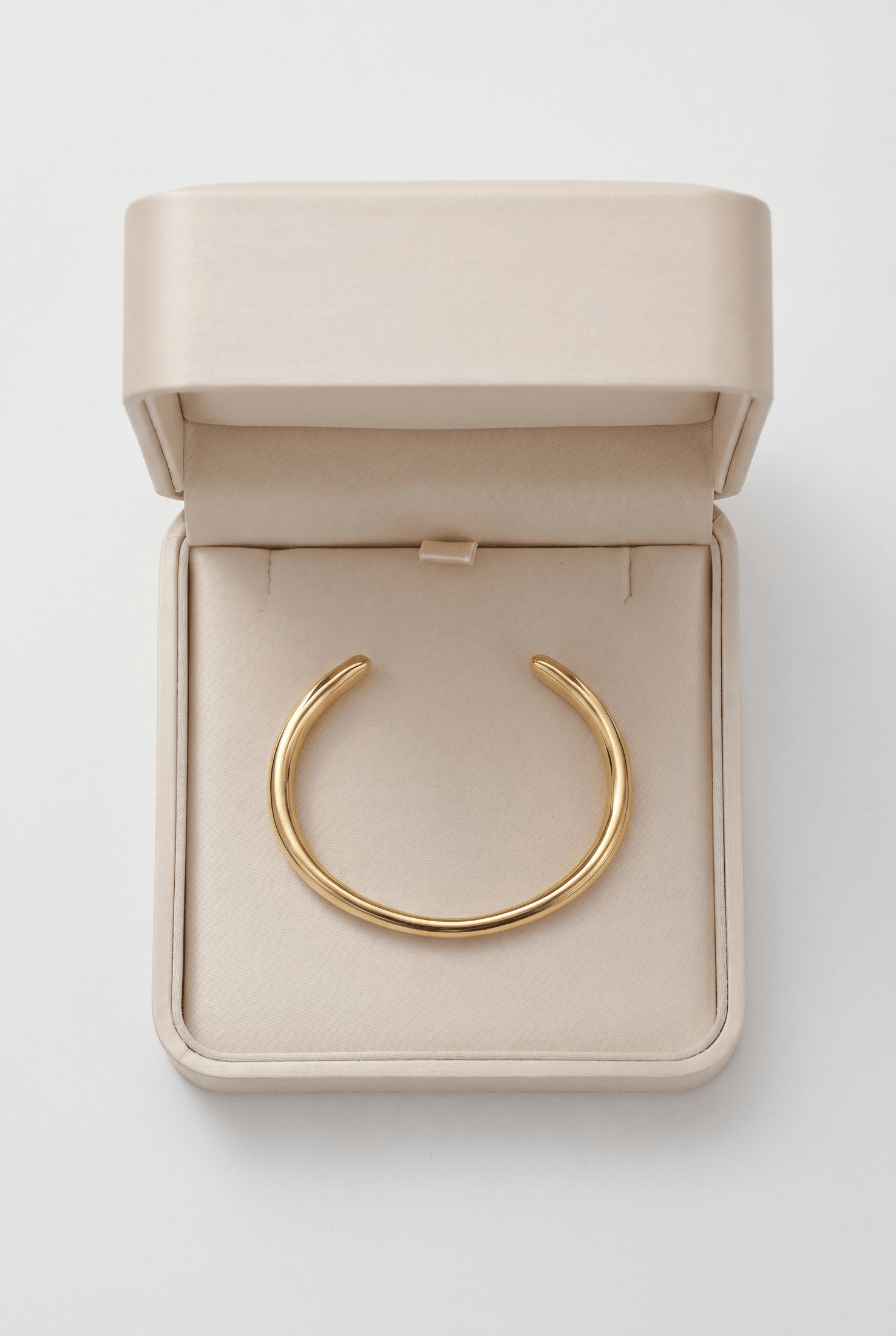 Minimalist gold cuff bracelet with a smooth, rounded finish, displayed in an open beige jewelry box.