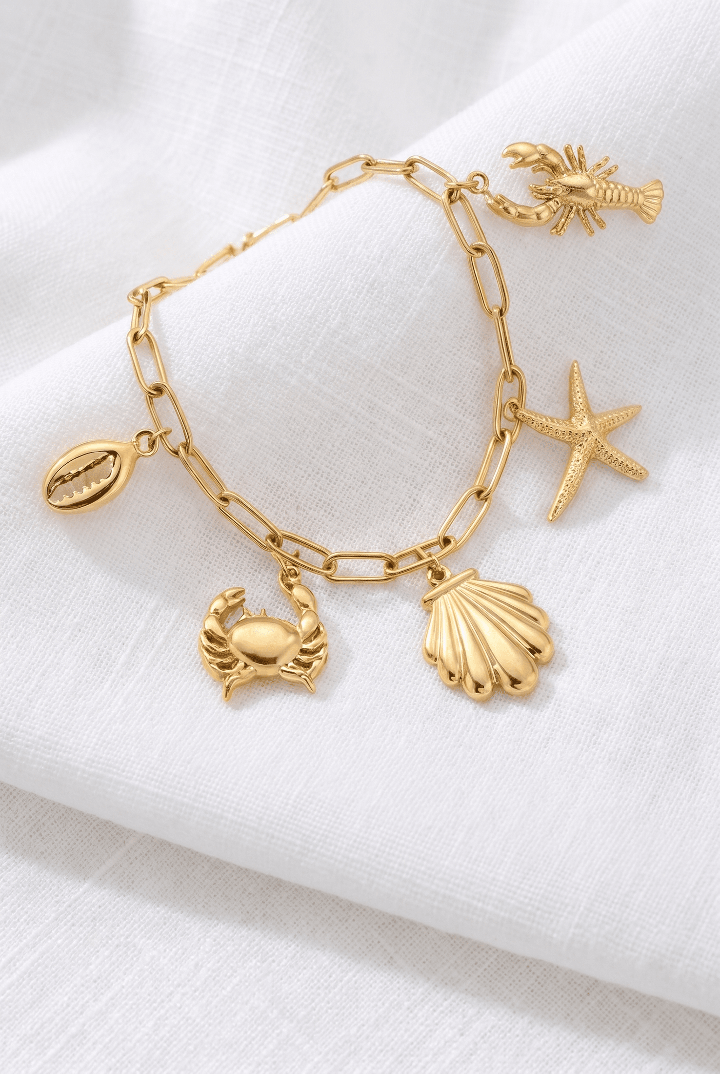 Gold link charm bracelet featuring sea-themed pendants: crab, starfish, seashell, lobster, and cowrie shell.