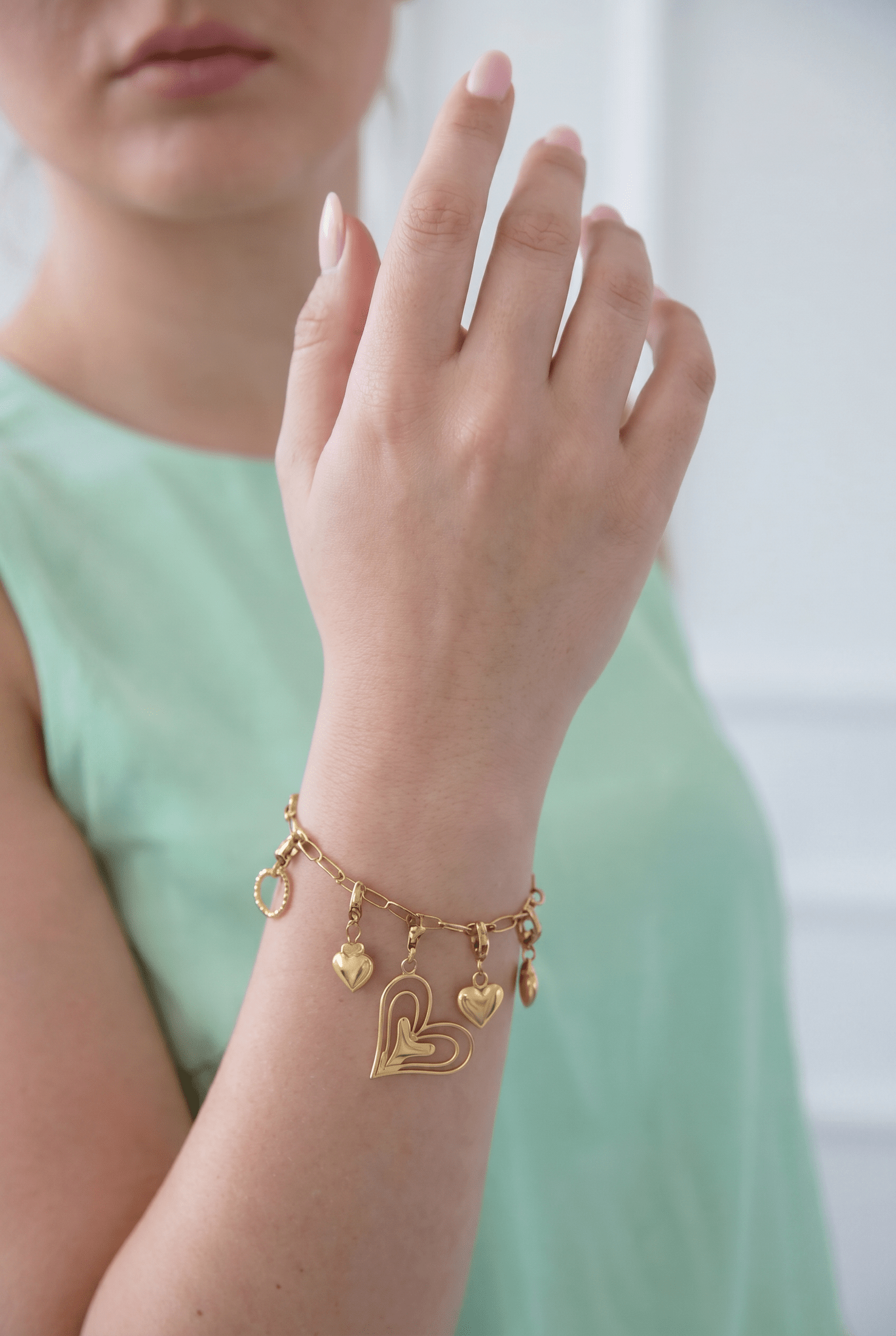 Gold charm bracelet on a wrist featuring multiple heart-shaped charms and an open-work heart centerpiece.