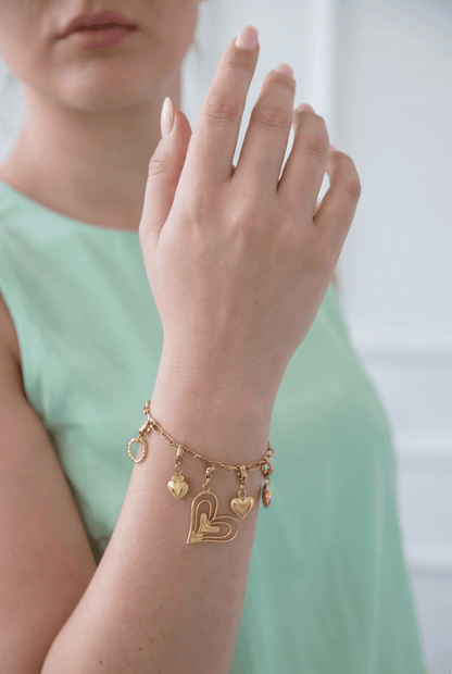 Gold charm bracelet on a wrist featuring multiple heart-shaped charms and an open-work heart centerpiece.