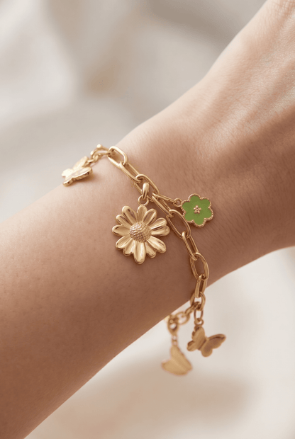 Gold link chain bracelet featuring dangling flower and butterfly charms, including a green enamel clover accent.
