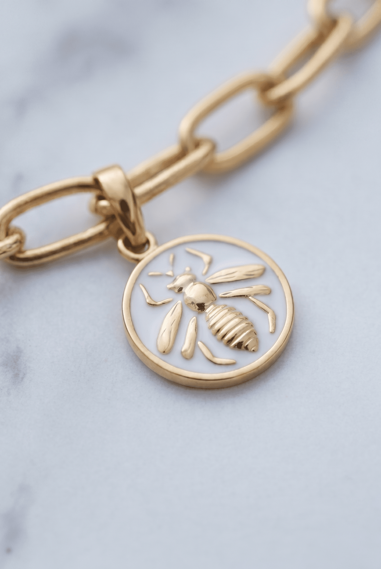 Gold-tone chain link bracelet featuring a round pendant with a white enamel inlay and a raised gold bee design.