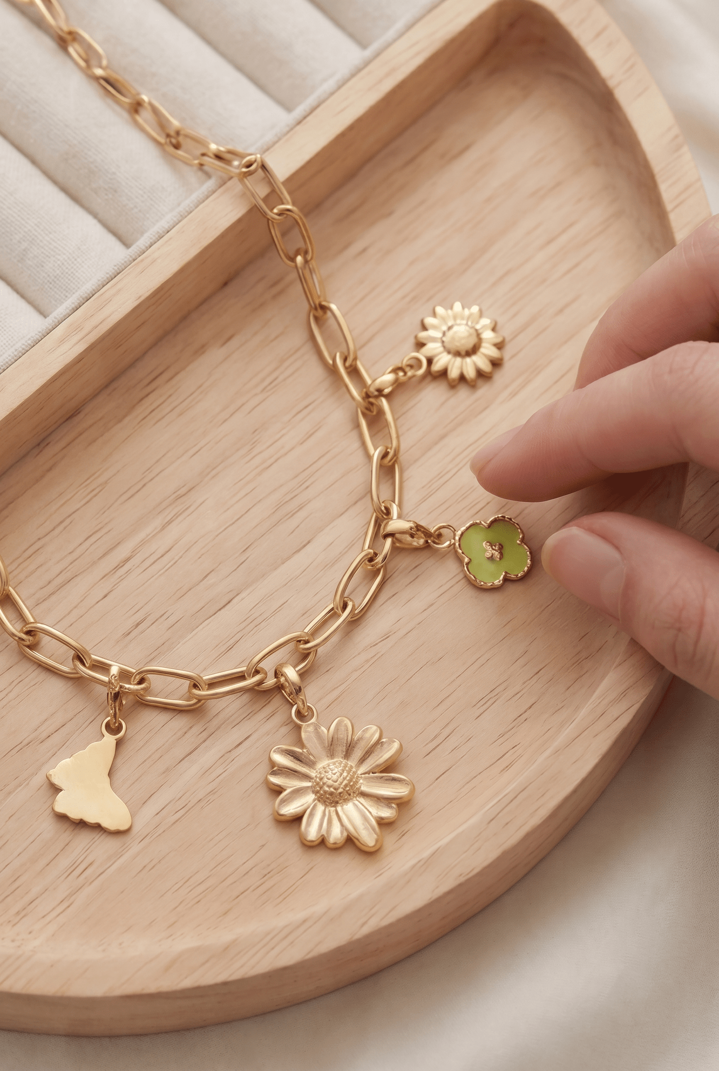 Gold-tone chain bracelet featuring dainty floral, butterfly, and green clover charms on a wooden tray.