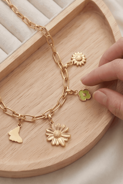 Gold-tone chain bracelet featuring dainty floral, butterfly, and green clover charms on a wooden tray.