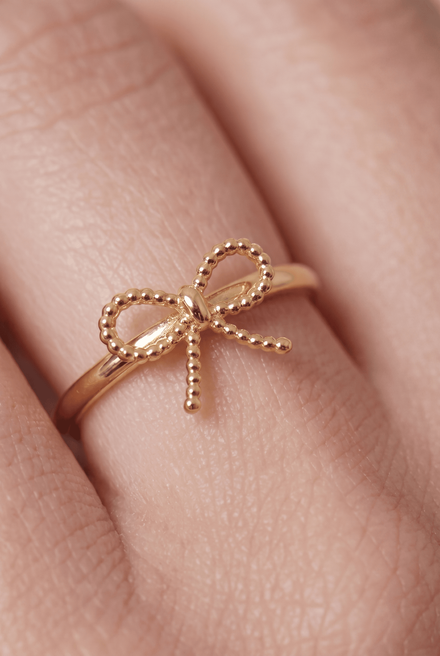 Dainty gold ring on a finger featuring a delicate, beaded bow design.