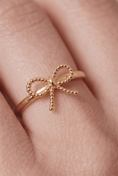 Dainty gold ring on a finger featuring a delicate, beaded bow design.