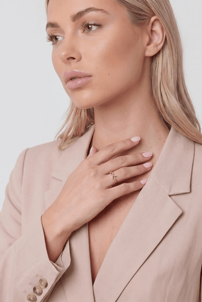 A woman wearing a dainty, polished gold bow-shaped ring on her finger.