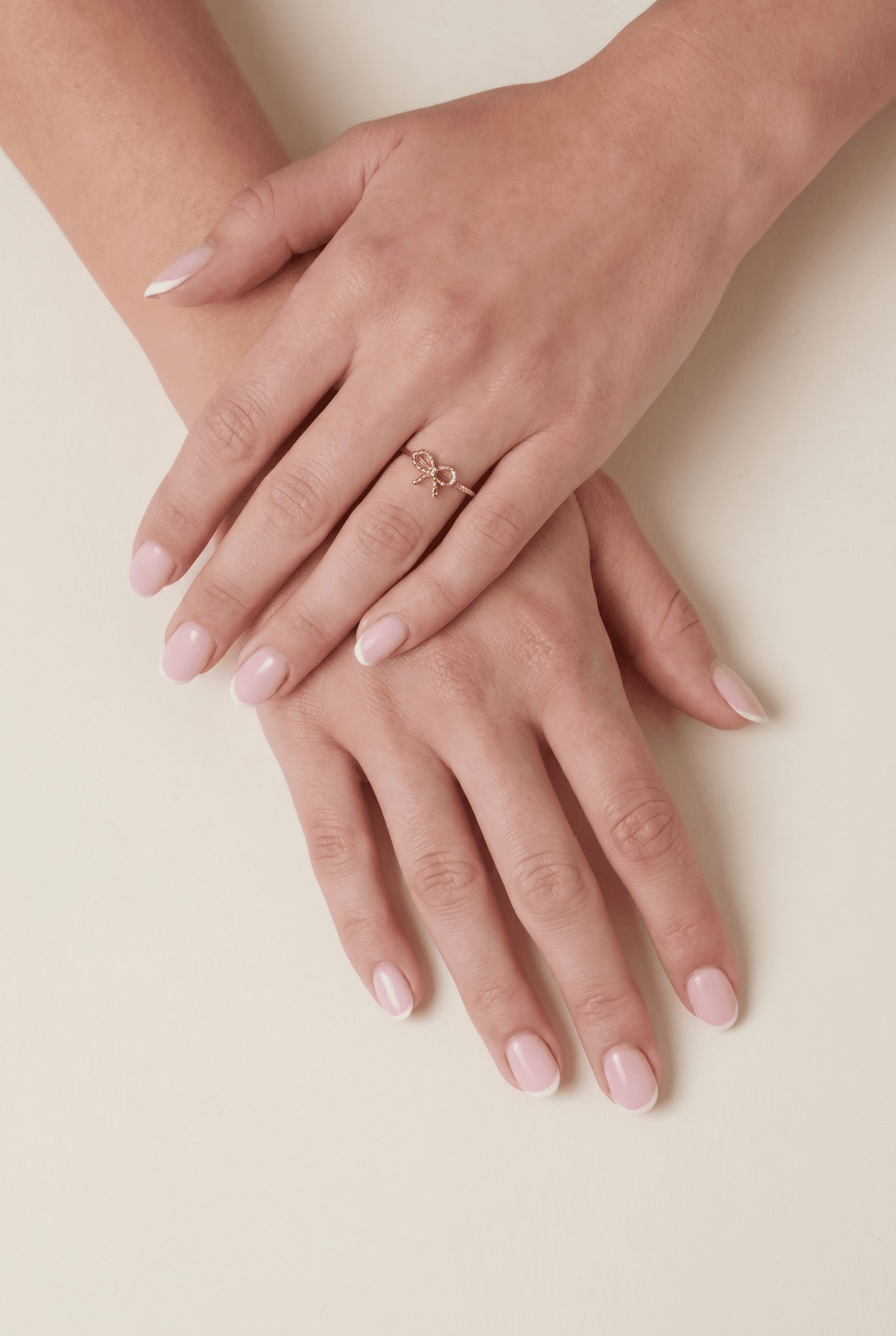 Dainty gold ring featuring a small, delicate bow design, worn on a hand with a classic French manicure.