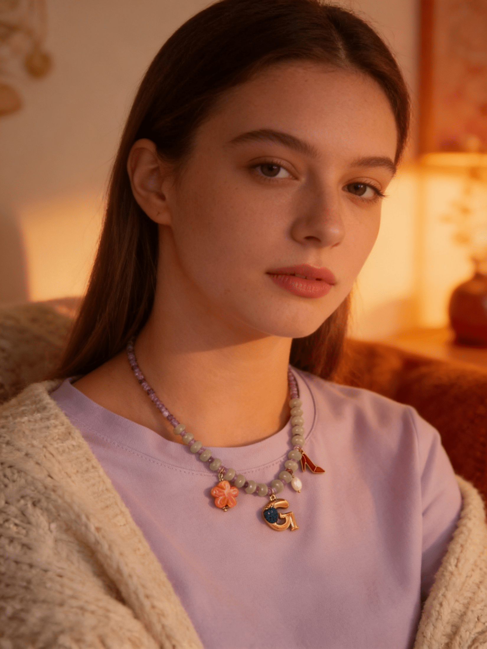 A beaded necklace with purple and green beads, featuring a gold letter 'G' charm, a pink flower, and a red shoe.