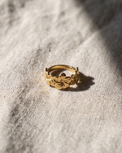 Chunky stainless steel hibiscus flower ring resting on light-colored weathered linen fabric under natural sunlight.