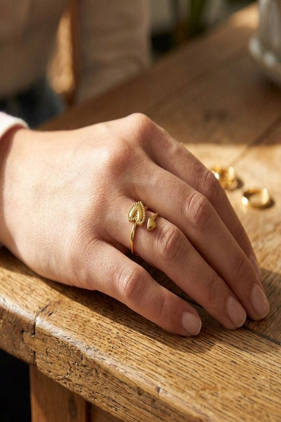 Full-hand shot of the Iconic Adjustable Stacker ring on a feminine hand resting on a wooden table, highlighting its elegant open design and fit.