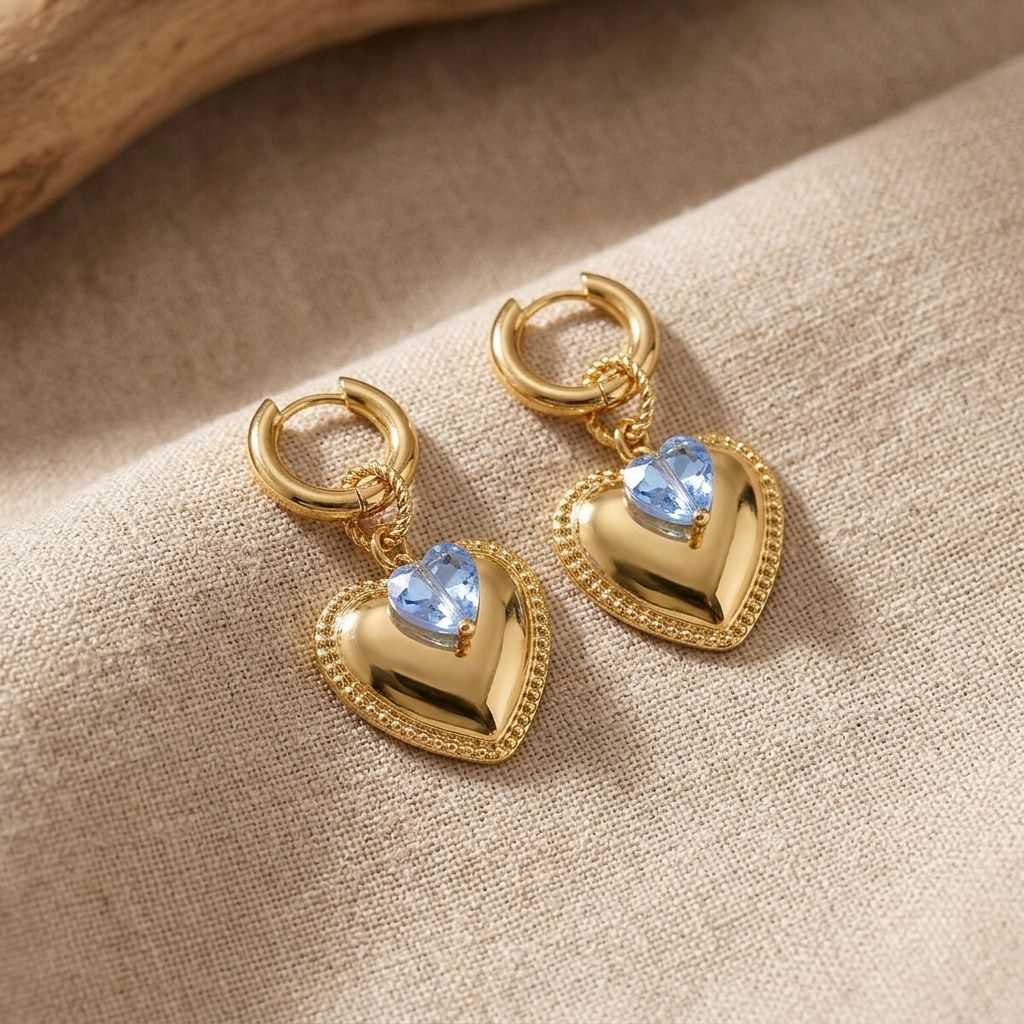 Heart-shaped stainless steel hoops with crystal accents displayed on beige linen, highlighting their shine and delicate design for casual wear.
