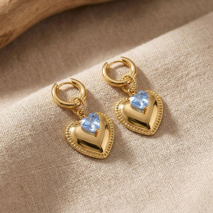 Heart-shaped stainless steel hoops with crystal accents displayed on beige linen, highlighting their shine and delicate design for casual wear.
