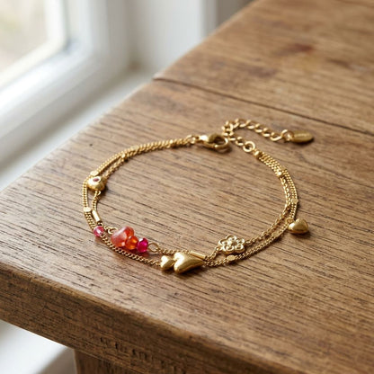 Close-up of layered heart charm bracelet with rhinestones and natural stones on wooden surface