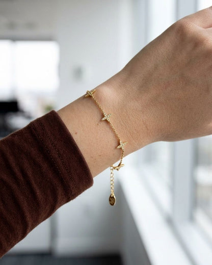 Dainty stainless steel chain bracelet featuring delicate clover motifs worn on a wrist in a bright professional office setting.