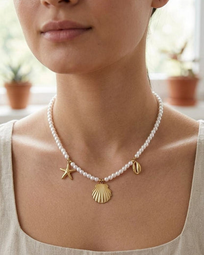 Small beaded necklace with imitation pearls and gold sea charms draped on a white ceramic bust in soft natural daylight.
