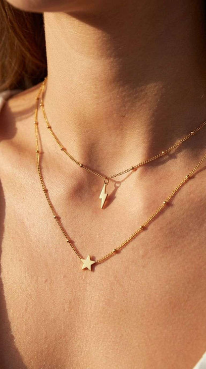 Lightning bolt pendant necklace on wood surface showing sleek stainless steel design and lobster clasp detail.