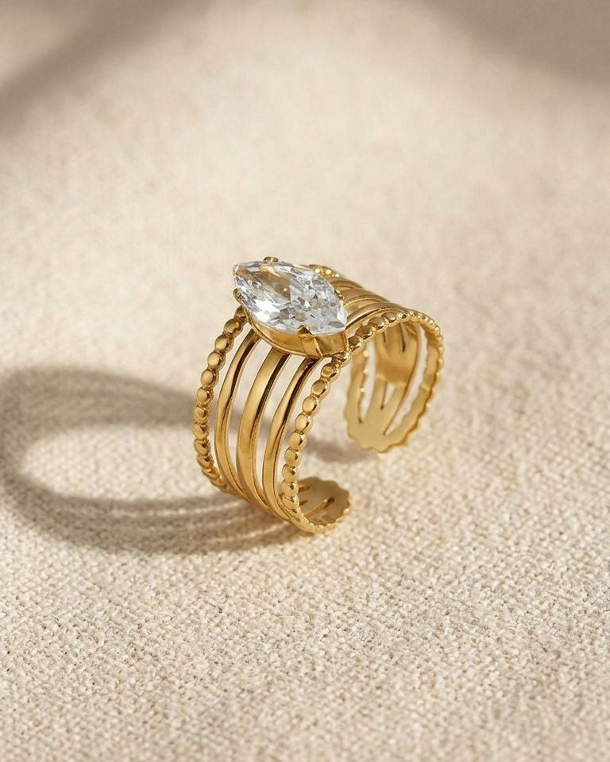 Close-up of the Marquise Gem Statement ring in gold-tone stainless steel with gemstone accents on textured beige fabric
