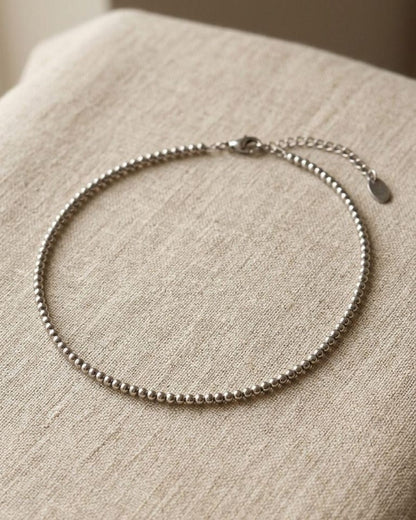 Close-up of delicate stainless steel beaded necklace with 5mm beads on a linen surface, highlighting its subtle shimmer and minimalist design.