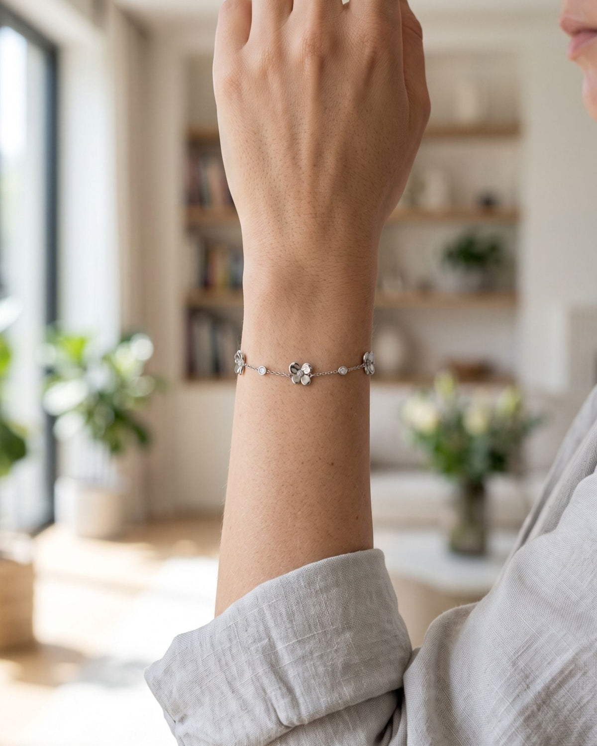 Dainty minimalist flower charm bracelet with a thin chain worn on a woman's wrist in natural daylight.