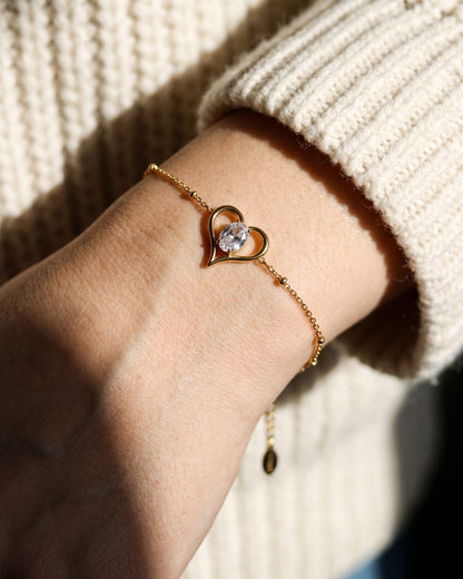 Close-up of a delicate minimalist heart charm bracelet worn on a model's wrist.