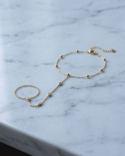 Petite rhinestone hand chain draped elegantly across a smooth, cool-toned marble surface.