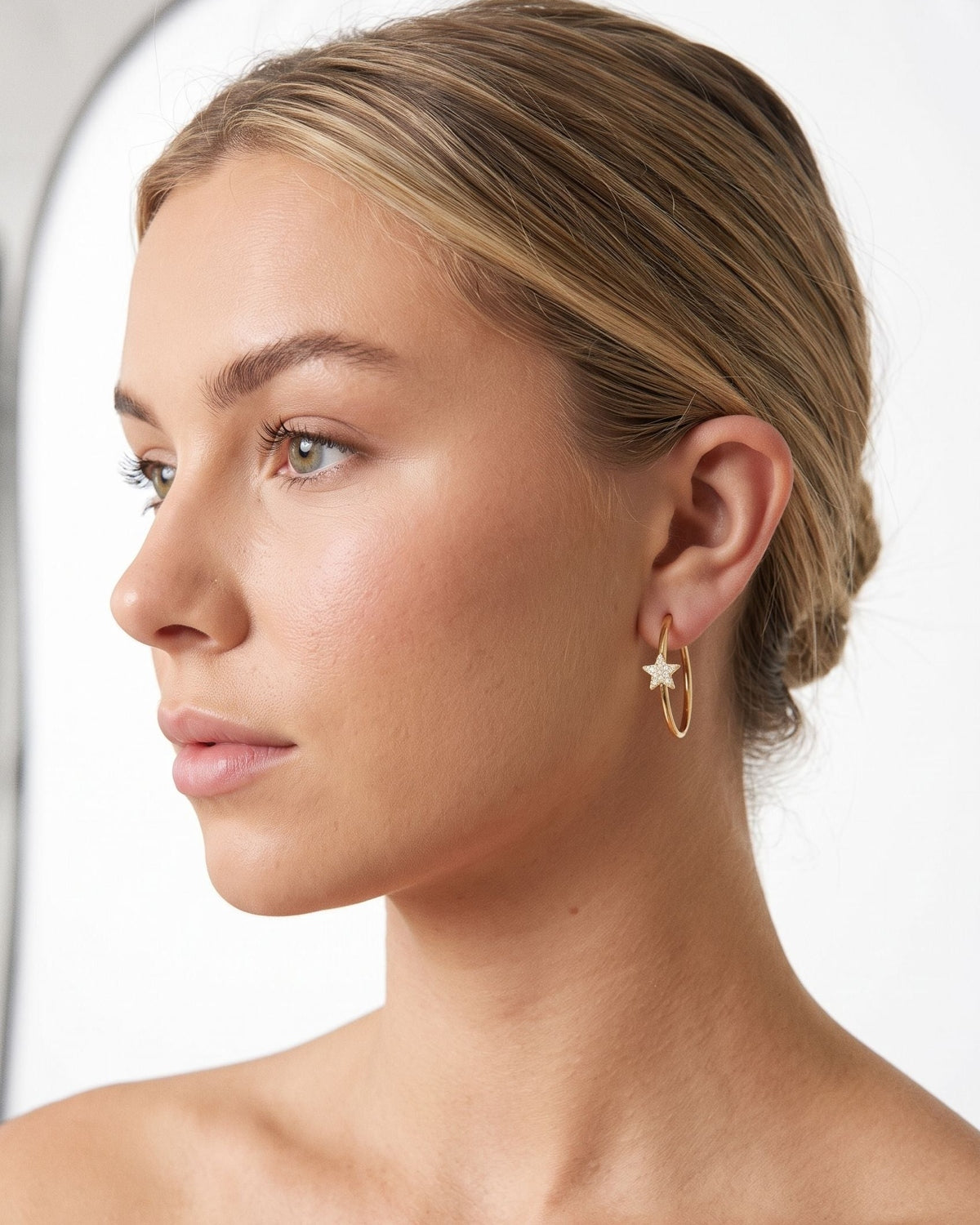 Minimalist star-shaped rhinestone hoop earrings worn by a model in a bright, clean studio setting.