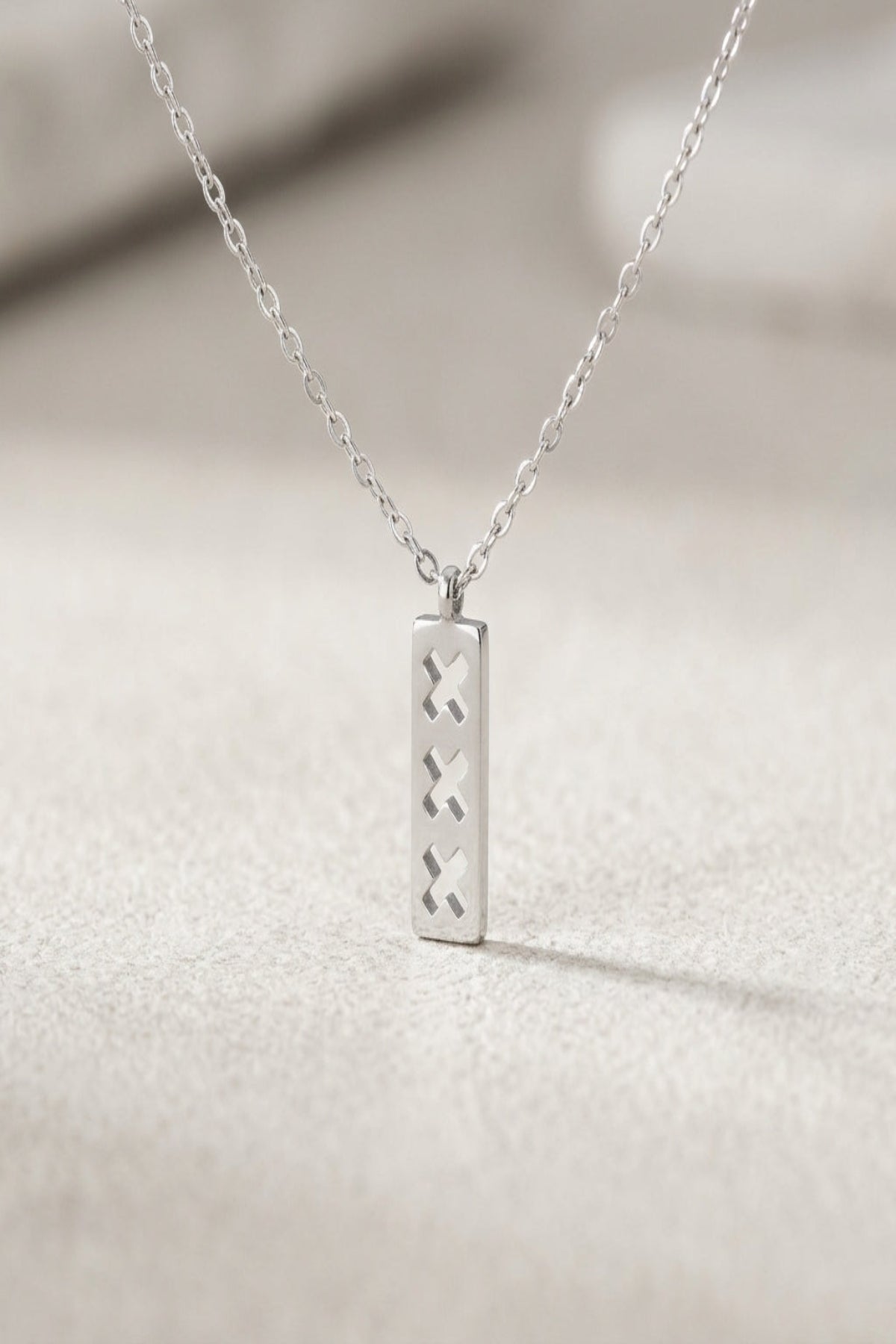 Close-up of minimalist triple X pendant necklace with rectangular pendant and cut-out X shapes in soft natural lighting.