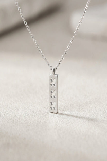Close-up of minimalist triple X pendant necklace with rectangular pendant and cut-out X shapes in soft natural lighting.