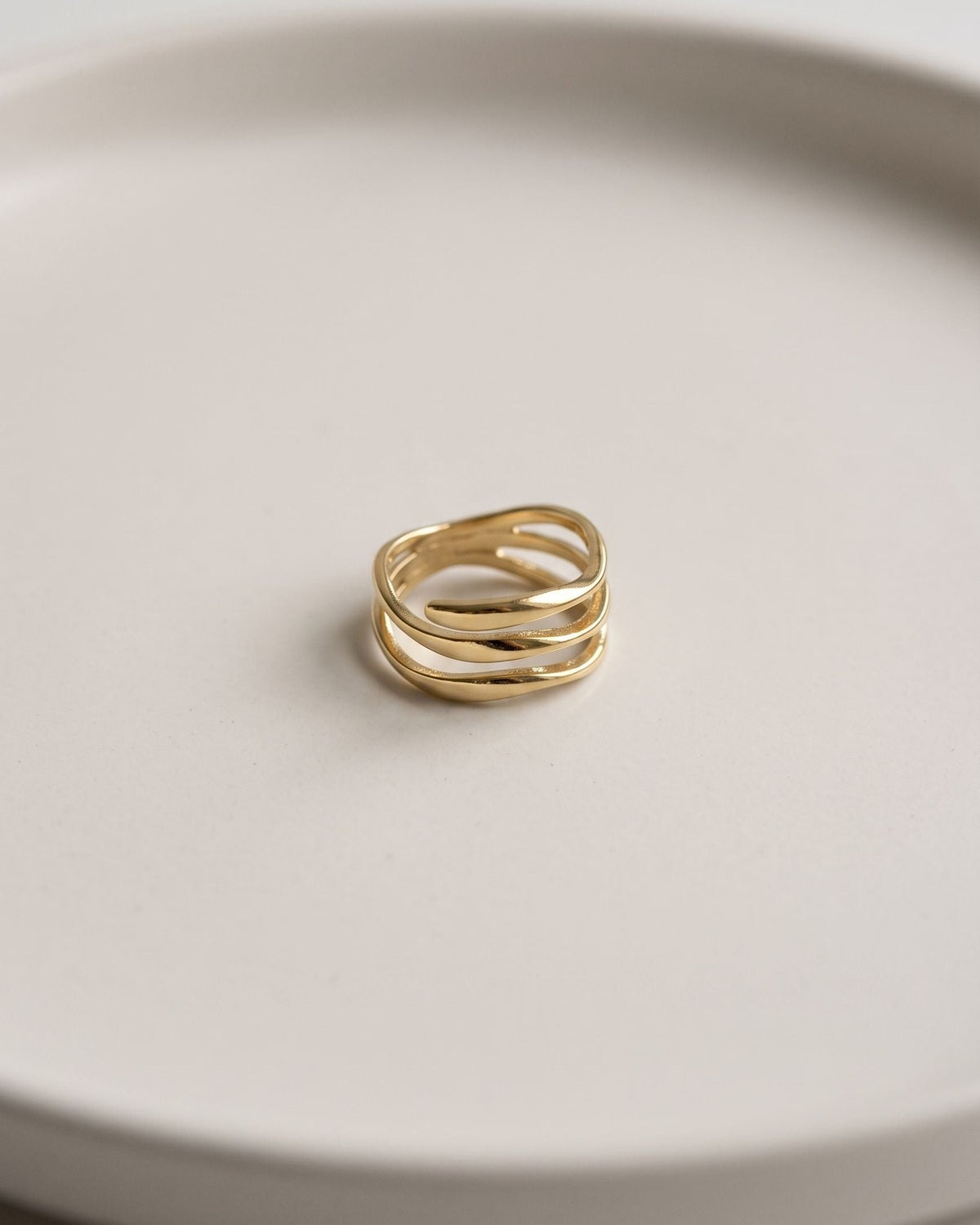 Delicate wave stack ring displayed on a clean matte ceramic surface with soft even lighting.