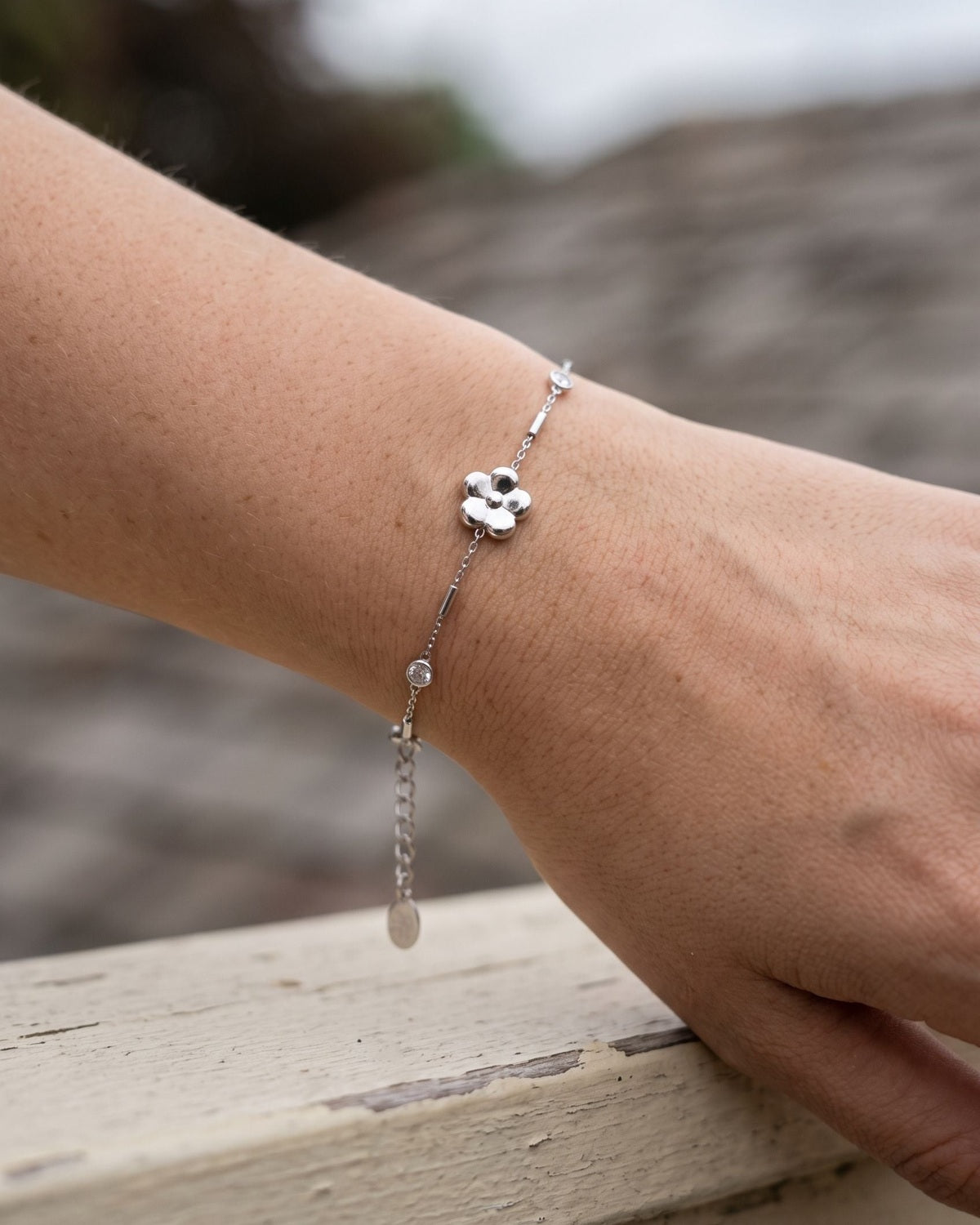 Elegant, petite stainless steel flower charm bracelet with zircon inlay worn on a model's wrist.