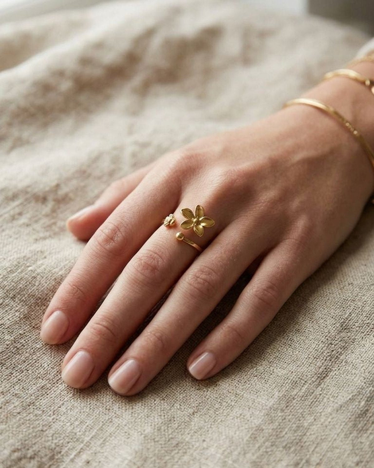 Model's hand with Gilded Petal Statement ring showcasing a delicate gold floral design on a linen fabric background.