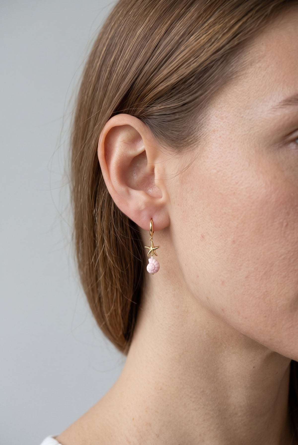 Side profile view of a woman wearing a petite gold shell and starfish charm earring.
