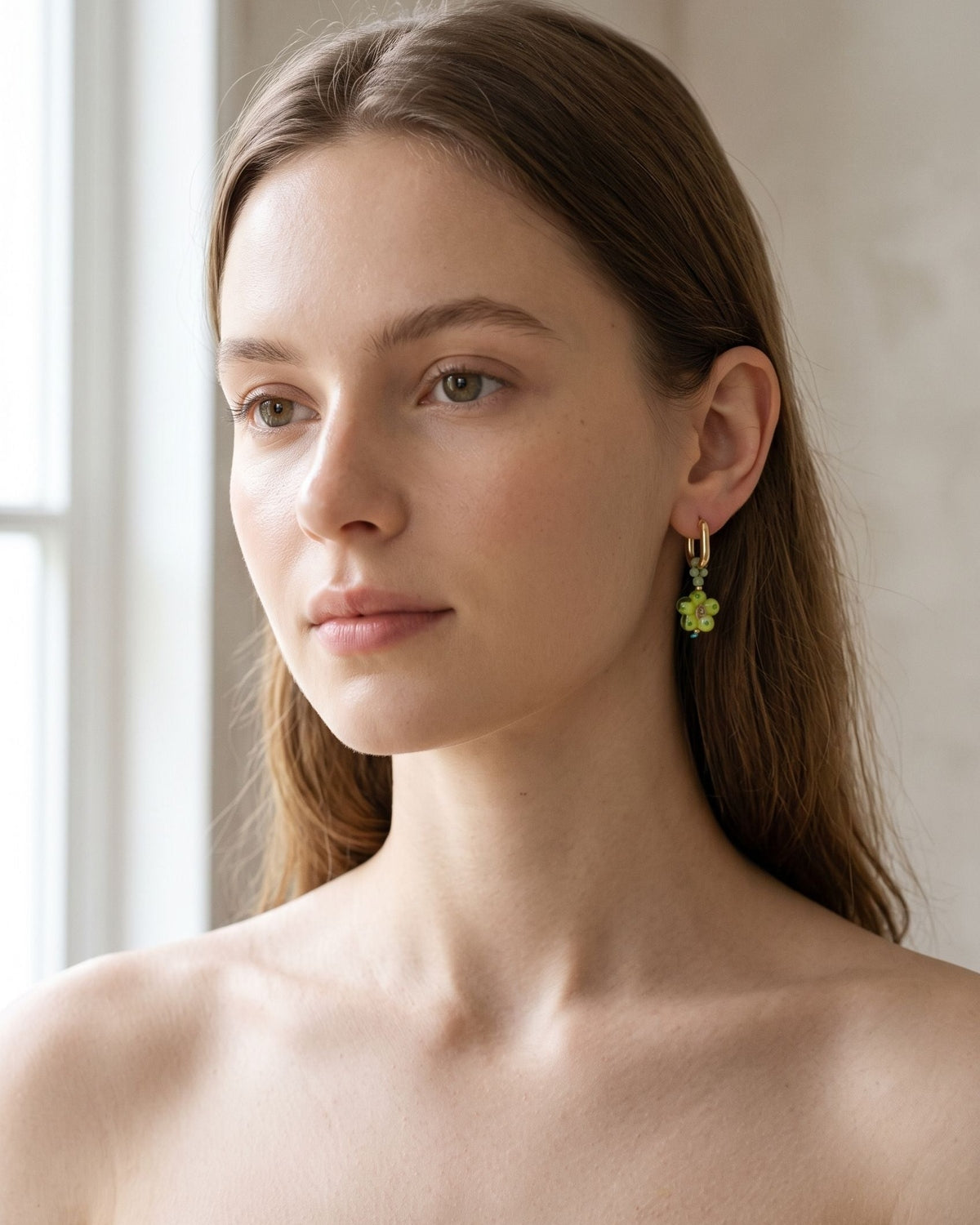 A model wearing subtle stainless steel hoop earrings with crystal flower pendants against a neutral background.