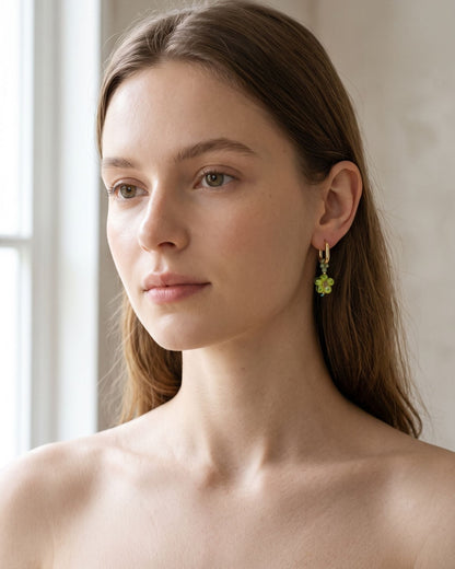 A model wearing subtle stainless steel hoop earrings with crystal flower pendants against a neutral background.