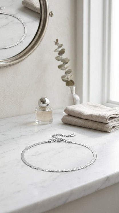 Minimalist silver-plated stainless steel necklace resting on white marble with natural window light, emphasizing its high-shine and elegant design.